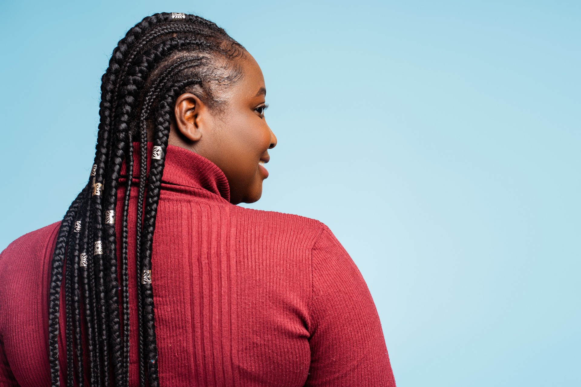 Back view smiling African American woman with stylish braided hair looking away. Hair salon
