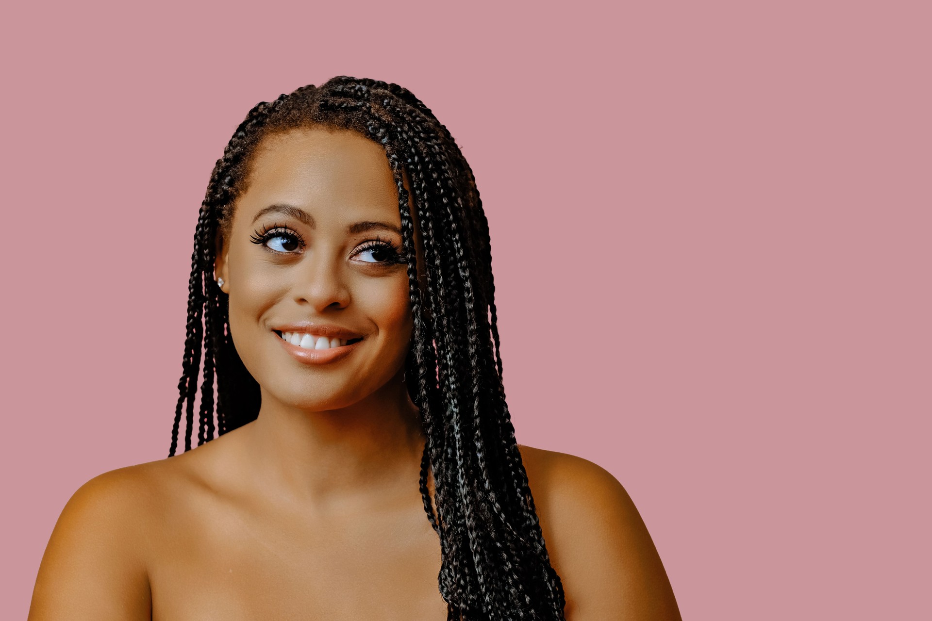beauty headshot of smiling young adult black woman braid hair on pink background looking away at copy space